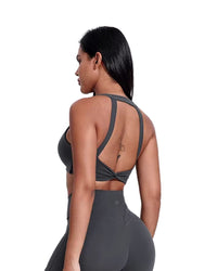 Woman wearing gray ORU LEGACY SPORTS BRA with wide straps and twist back design, breathable seamless fabric.