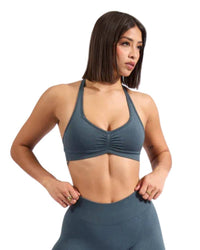 Woman wearing gray ORU halter sports bra with sweetheart neckline and inverted V hemline, light to medium support activewear.